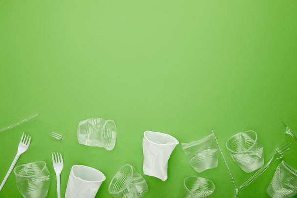 top view of crumpled plastic cups and forks on green background with copy space - Photo, Image