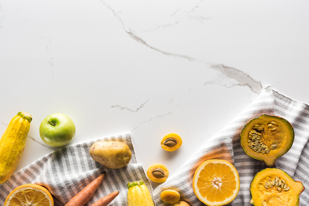 pohled na pruhovaný ručník s dýní, meruňky, bramborem, cuketou, mrkví a oranžovým povrchem na mramorové ploše - Fotografie, Obrázek