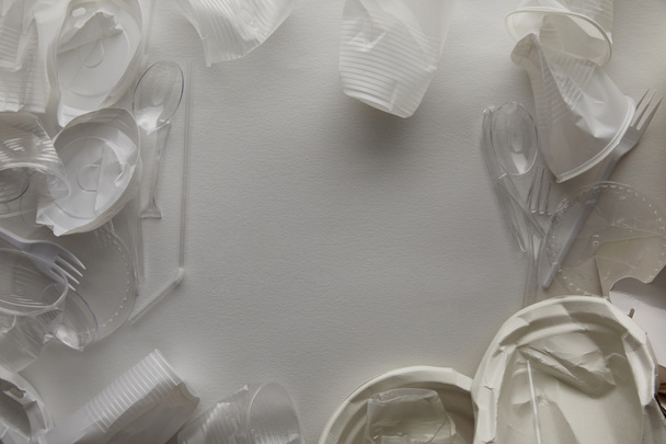 Κορυφαία όψη των τσαλακωμένες πλάκες μίας χρήσης, πλαστικά κύπελλα, πιρούνια και κουτάλια σε λευκό φόντο με χώρο αντιγραφής - Φωτογραφία, εικόνα