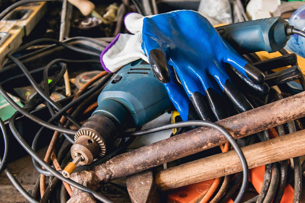 Un taladro eléctrico y guantes azules se encuentran en una pila de cable y martillos
. - Foto, imagen