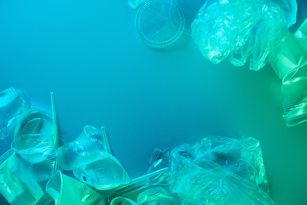 vista superior de sacos de plástico amassados, copos, palhas e garfos em luz azul
 - Foto, Imagem