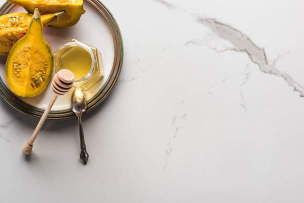 Κορυφαία όψη της πλάκας με κολοκύθα και μέλι και κουτάλι σε μαρμάρινη επιφάνεια - Φωτογραφία, εικόνα