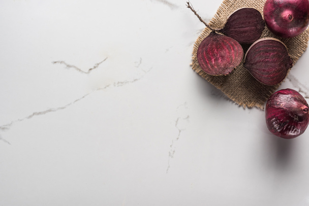 top view of red onions and beetroot halves on marble surface with hessian - Фото, изображение