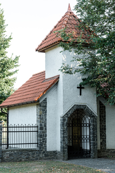 groene bomen in de buurt van christelijke kerk met rood dak en metalen hek  - Foto, afbeelding