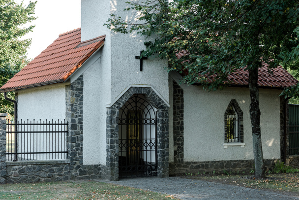 drzew w pobliżu Kościoła chrześcijańskiego z czerwonym dachem i metalicznym ogrodzeniem  - Zdjęcie, obraz