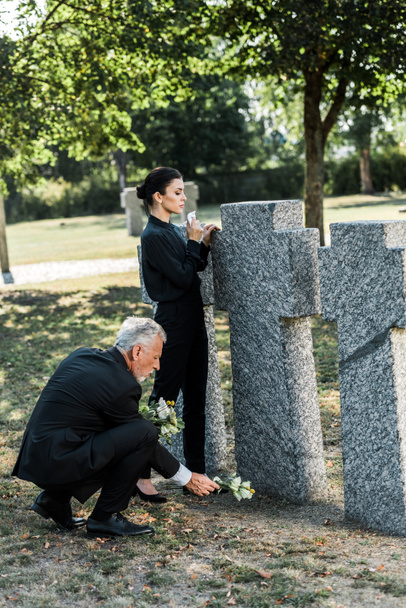 hombre mayor poniendo flores cerca de tumbas y mujeres en el cementerio
  - Foto, Imagen