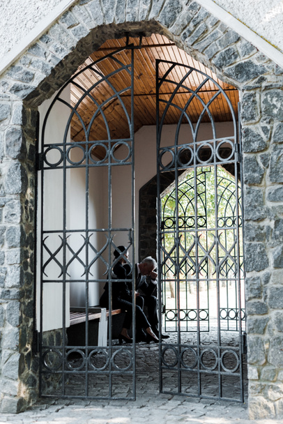 hombre y mujer molestos sentados cerca de puertas metálicas en el cementerio
  - Foto, Imagen