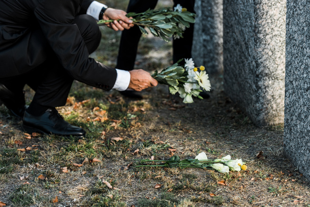 vista recortada del hombre mayor poniendo flores cerca de tumbas
  - Foto, Imagen