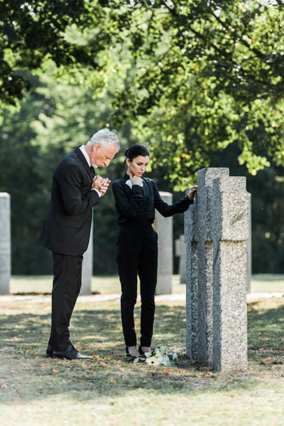 upset man with grey hair and attractive woman standing near tombstones - Fotografie, Obrázek