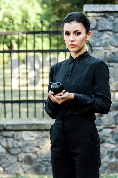 atraente mulher olhando para a câmera enquanto segurando preto porquinho banco
  - Foto, Imagem