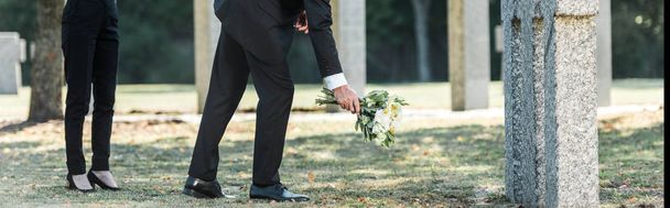 墓石と女性の近くに花を置く男のパノラマショット  - 写真・画像