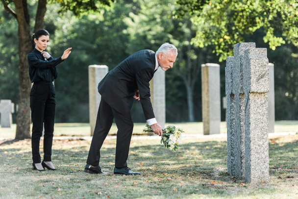 man with grey hair putting flowers near tombstones and woman  - Zdjęcie, obraz