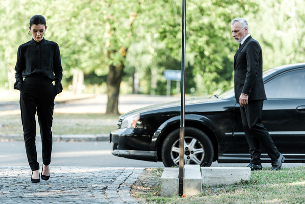 upset man and sad woman in formal wear walking near black car  - Foto, Bild