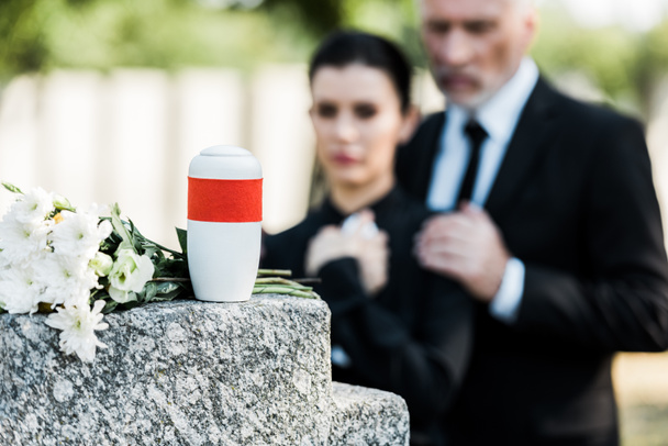 selective focus of white flowers near mortuary urn and two people  - Foto, imagen