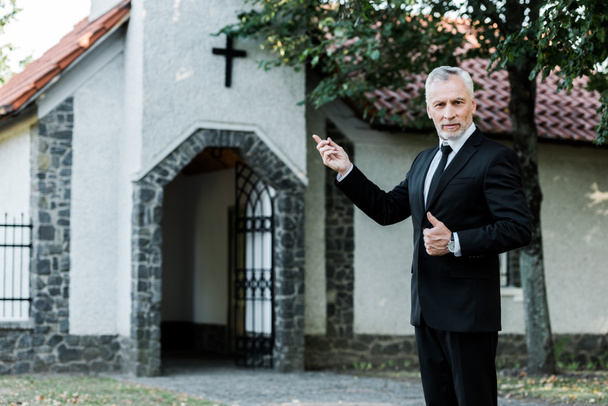 uomo anziano mostrando pollice verso l'alto e puntando con il dito alla chiesa
  - Foto, immagini