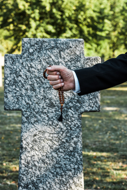 vue recadrée d'un homme âgé tenant des perles de chapelet près de la pierre tombale
   - Photo, image