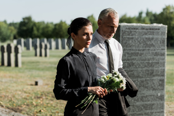 bärtiger Mann mit grauen Haaren geht bei Beerdigung neben Frau mit Blumen - Foto, Bild