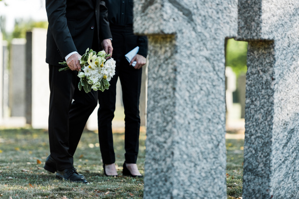 cropped view of man standing near woman with flowers near tombs  - Zdjęcie, obraz