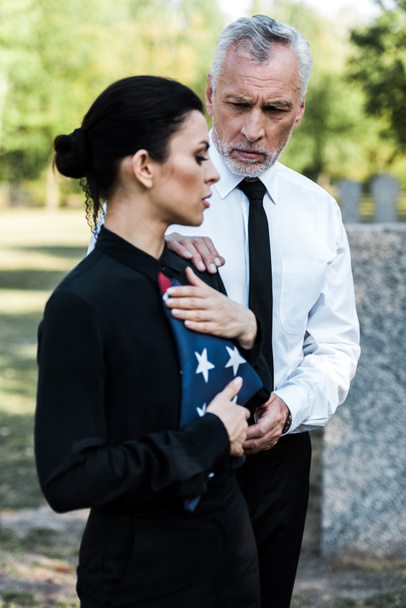 selective focus of bearded man looking at woman with american flag on funeral  - Photo, Image