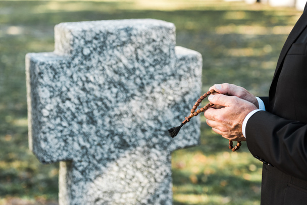 cropped view of man holding rosary beads near tombstone   - Zdjęcie, obraz