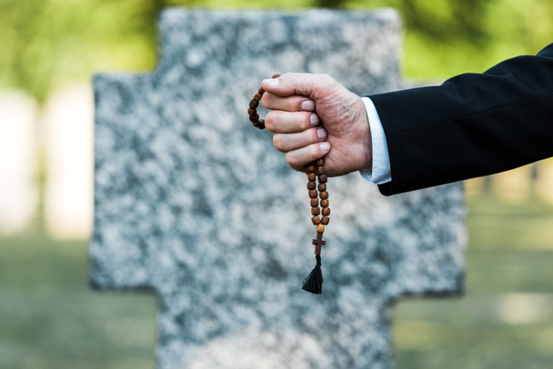 обрезанный вид пожилого человека, держащего четки возле надгробия
   - Фото, изображение