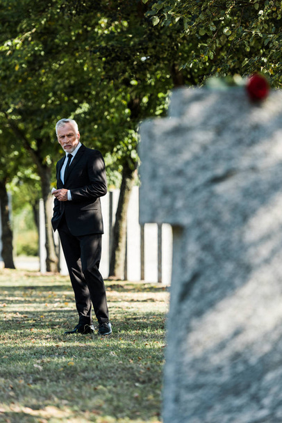 selective focus of upset elderly man standing on graveyard  - Photo, Image