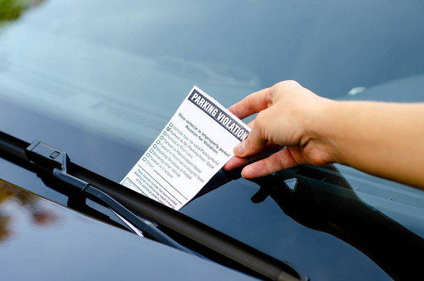 Close-up de uma mulher tomando bilhete de estacionamento no pára-brisas do carro
 - Foto, Imagem