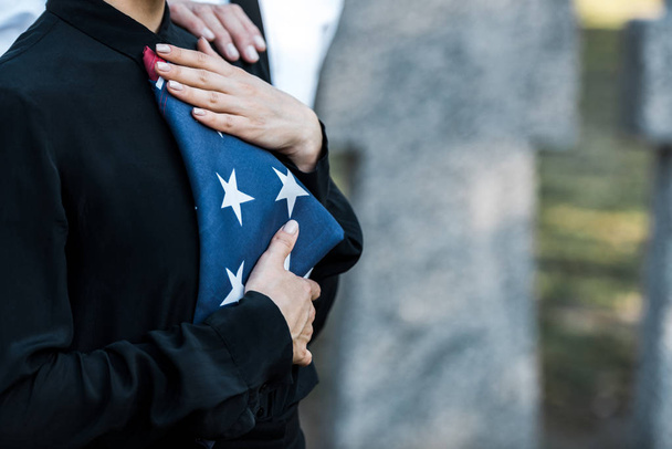 墓地でアメリカ国旗を持つ女性のトリミングされた眺め  - 写真・画像