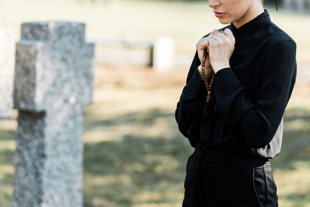墓石の近くにロザリオビーズを持つ女性のトリミングされたビュー - 写真・画像