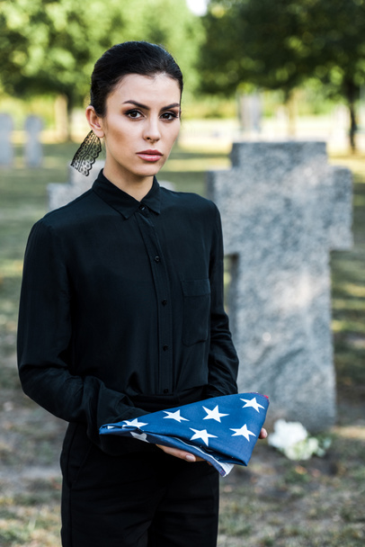 attractive woman holding american flag on graveyard  - Zdjęcie, obraz