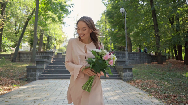 junge Frau mit Blumenstrauß läuft nahe Treppe im Park - Filmmaterial, Video