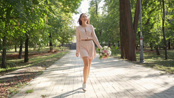 happy girl with bouquet walking on pavement in park - Кадры, видео