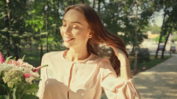 Szczęśliwa młoda kobieta z kwiatami chodzenie w parku - Materiał filmowy, wideo