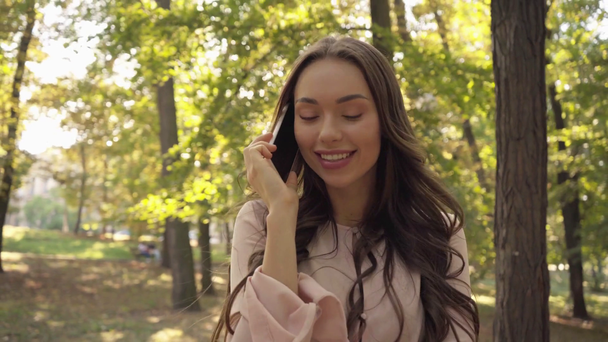 young woman talking on smartphone in park - Materiał filmowy, wideo