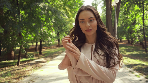fiatal nő nézi a kamerát, és mosolyogva parkban - Felvétel, videó