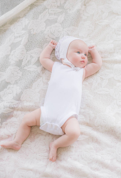 Cute toddler baby in white clothes lies on a white bed at home - Photo, image
