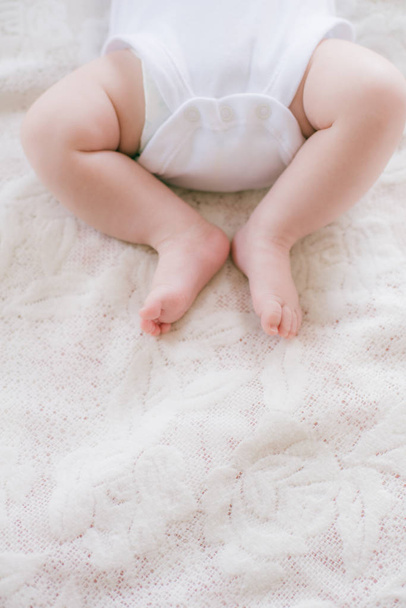 Little legs of a baby lying on a white bed at home. Happy motherhood. - Valokuva, kuva
