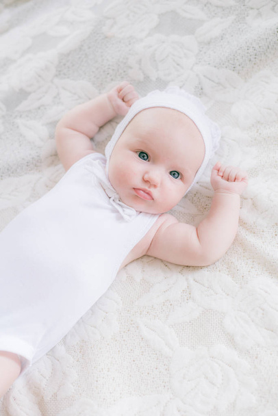 白い服を着たかわいい幼児の赤ちゃんは、自宅で白いベッドの上に横たわっています - 写真・画像