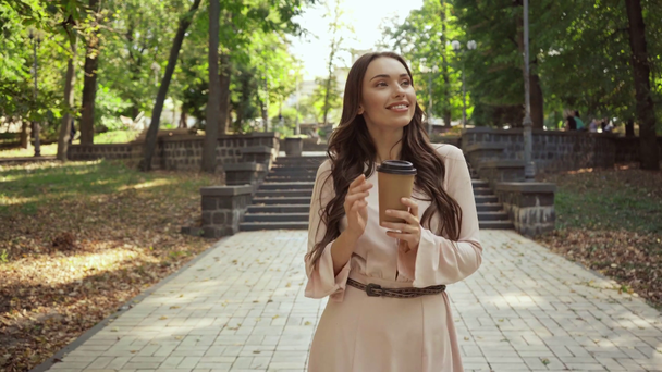 mladá žena s kávou, aby šla pěšky blízko schodů v parku - Záběry, video