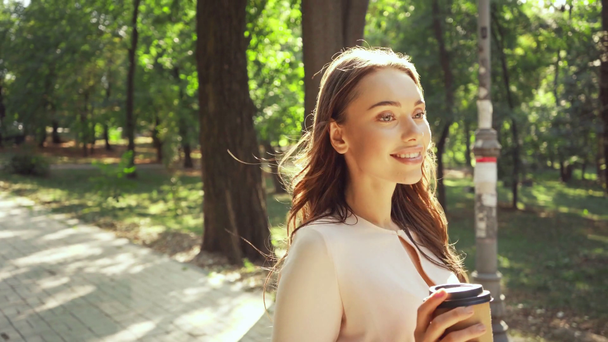 Młoda kobieta z kawą iść pieszo w parku - Materiał filmowy, wideo