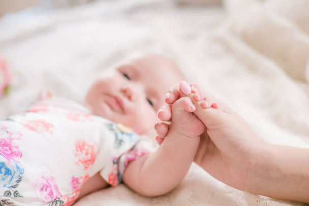 Mom's hands are holding a little cute hand of a newborn daughter at home on a white bed. Happy motherhood - Foto, imagen