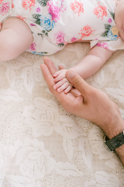 Mom's hands are holding a little cute hand of a newborn daughter at home on a white bed. Happy motherhood - Foto, Imagem