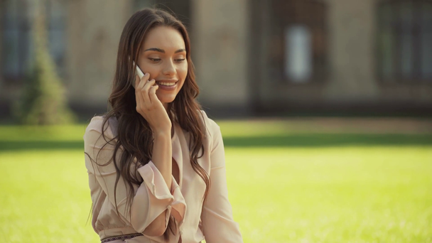 молода жінка розмовляє на смартфоні і сидить на траві
 - Кадри, відео