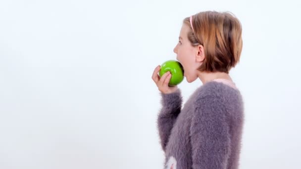 Ein junges Mädchen beißt in einen grünen Apfel. sie wird von der Kamera abgewendet. - Filmmaterial, Video