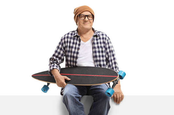 Mature man with a longboard sitting on a panel  - Foto, immagini