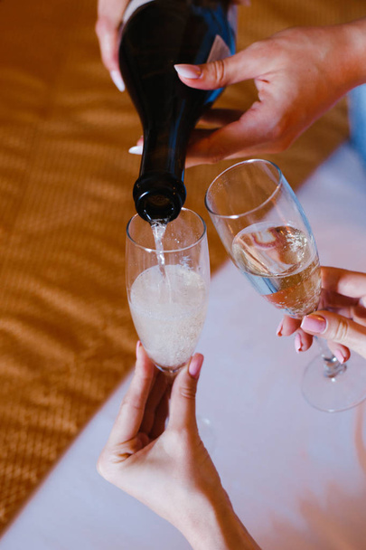 woman pours champagne into two glasses held by another woman - Fotó, kép