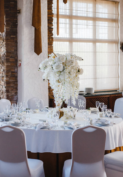 τραπέζι στρογγυλής τραπέζης, διακοσμημένο με ένα μπουκέτο λευκά λουλούδια στο κέντρο των πινάκων - Φωτογραφία, εικόνα