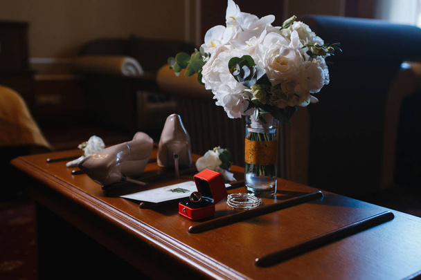 bruiloft accessoires: bruids boeket, twee knoopsgaten, vrouwen schoenen, trouwringen in een doos, vrouwen armband, envelop met een bruiloft uitnodiging - Foto, afbeelding