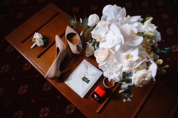 свадебные аксессуары: свадебный букет, две пуговицы, женская обувь, обручальные кольца в коробке, женский браслет, конверт с приглашением на свадьбу
 - Фото, изображение