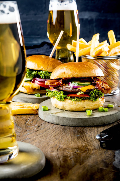 close-up view of glasses of beer, fresh tasty burgers and french fries on table - 写真・画像